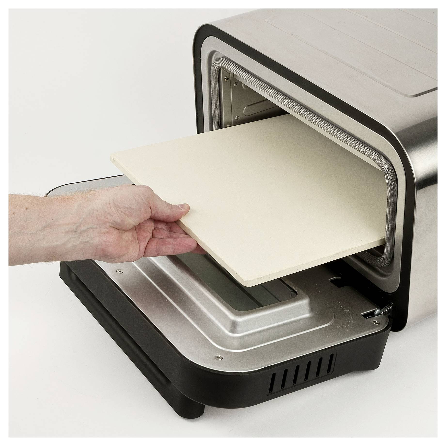 Hand placing a pizza stone into an open tabletop oven or pizza oven.