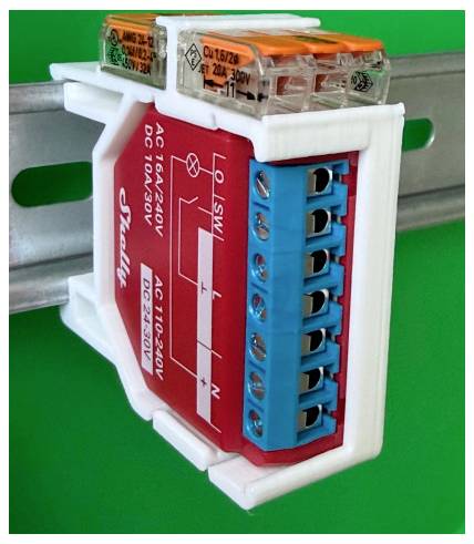 Close-up of a red and blue electrical connector or relay module mounted on a metal rail with terminal openings and printed voltage labels.