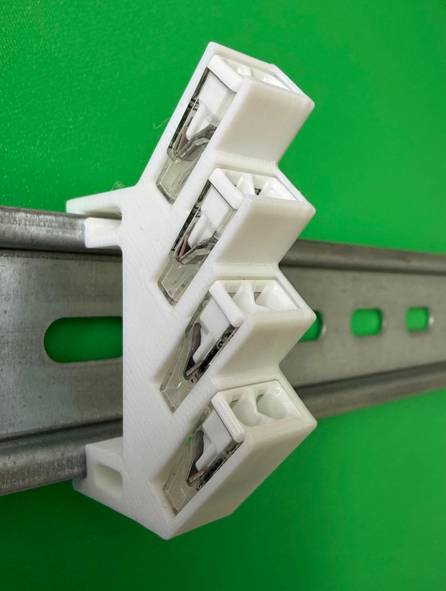 White electrical terminal block clipped onto a metal DIN rail against a green background.<br>
