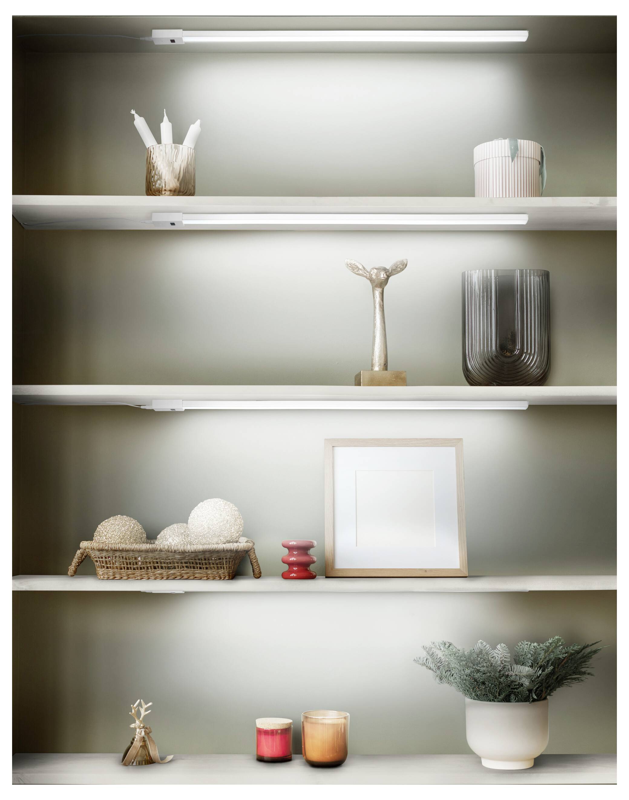 Minimalist shelving display with small decorative objects: baskets, candle holders, framed print, vase, and plant under shelf lights.