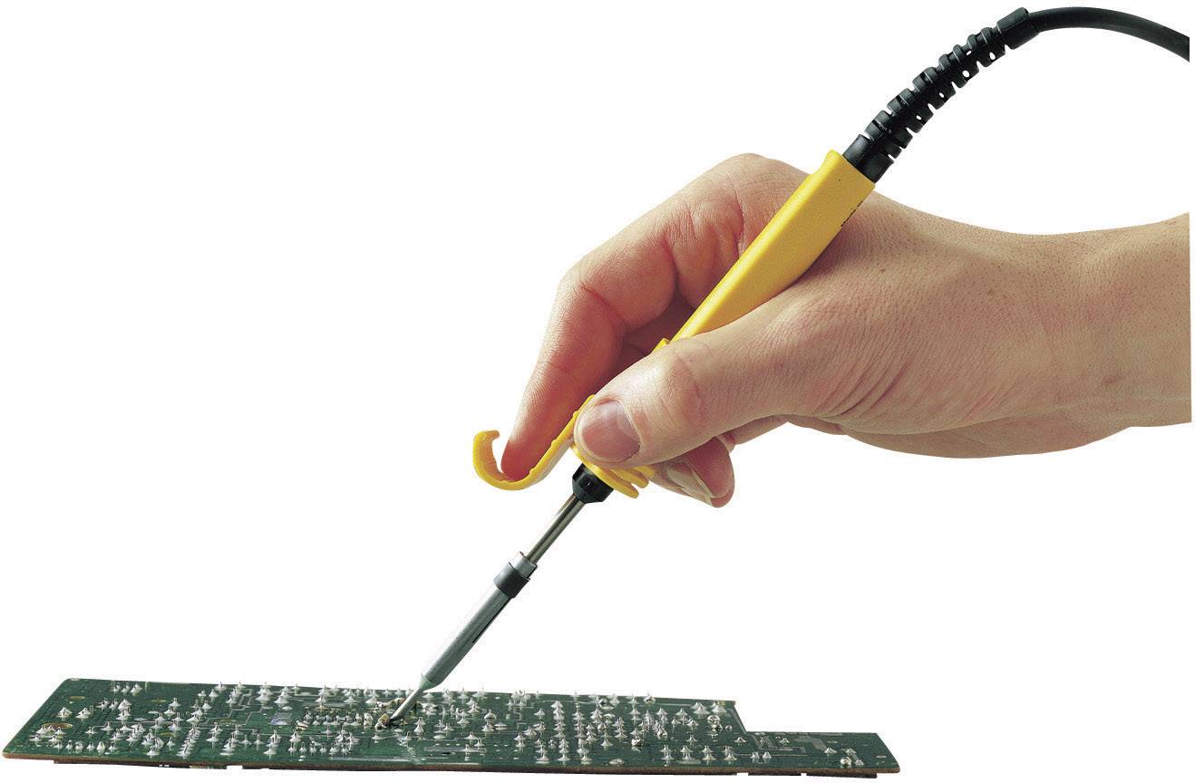 A hand is holding a soldering iron and soldering on a green circuit board with numerous electronic components.