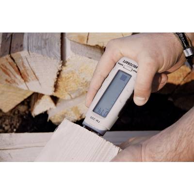 A hand is holding a wood moisture metre, displaying a reading of '21.2%'. Split logs can be seen in the background.