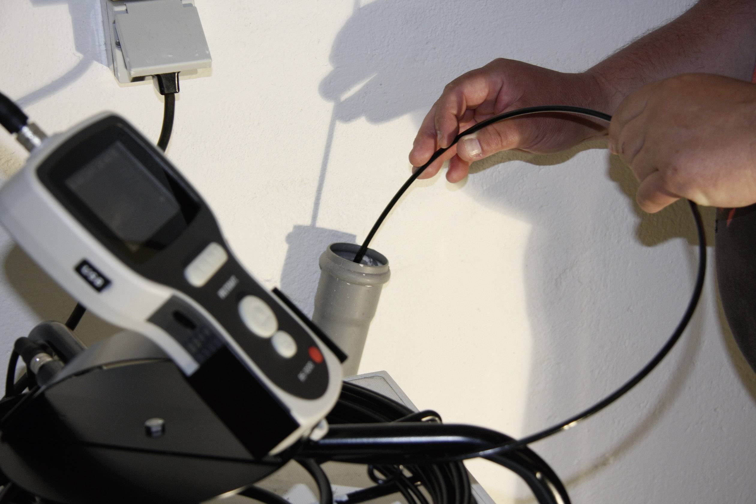 A person is holding a black cable connected to an electronic measuring device in a bright room.