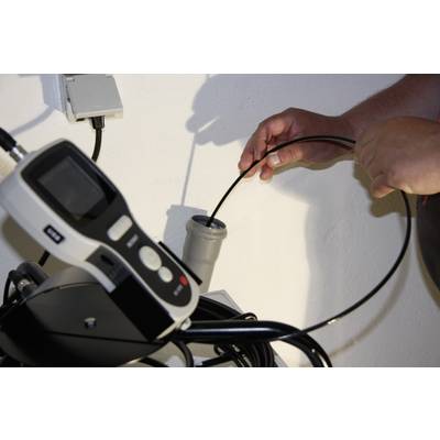 A person is holding a black cable connected to an electronic measuring device in a bright room.