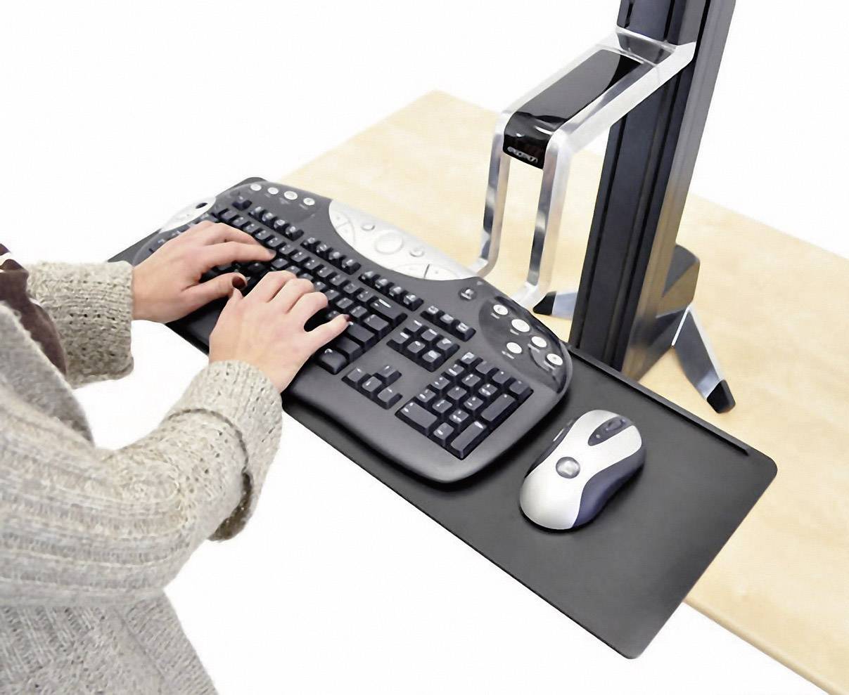 A person is working on a computer with a black keyboard and mouse at an adjustable desk.