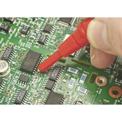 A hand operates a red test probe on a green circuit board to test or measure electronic components.