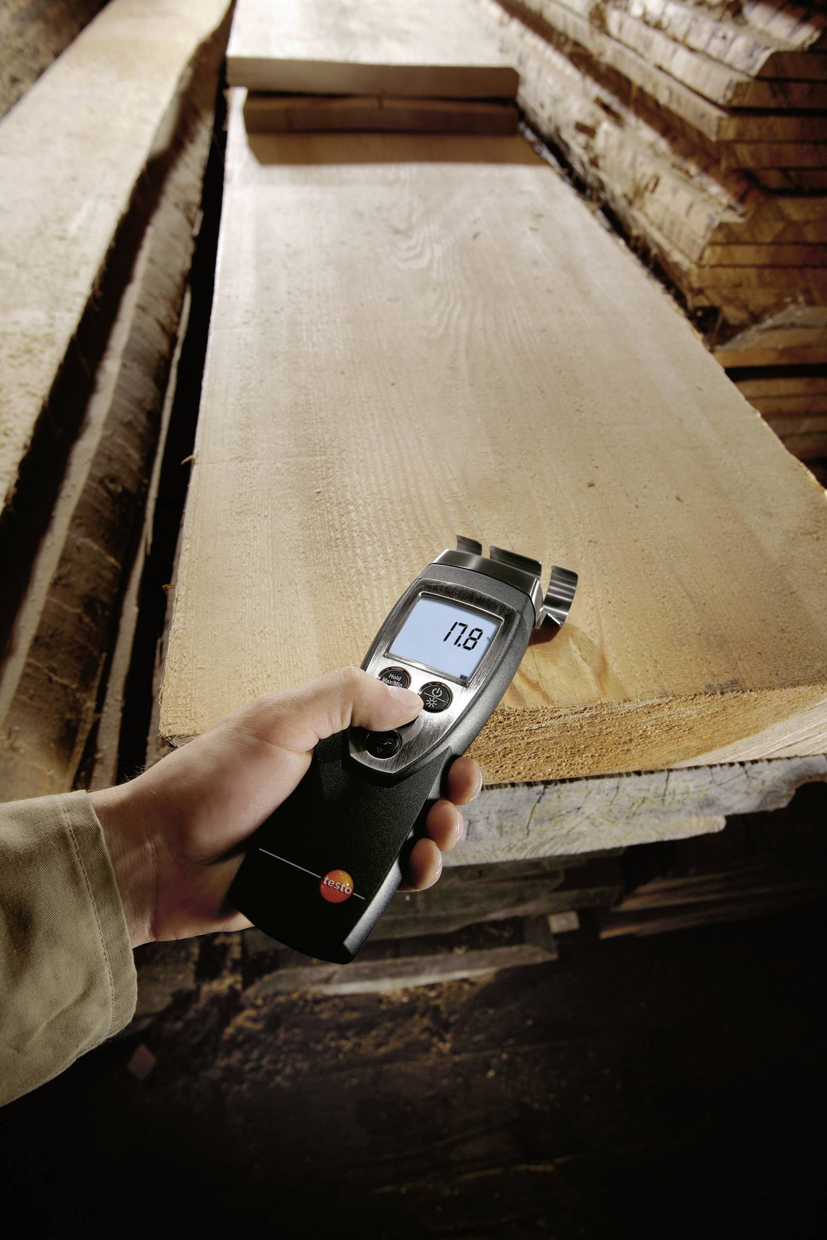 A person is measuring the moisture content of a large wooden board with a digital measuring device showing '7.8'.
