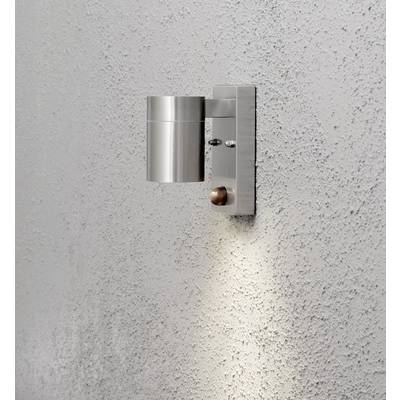 A modern, cylindrical exterior light made of metal is mounted on a grey, textured wall and illuminates the area beneath it.
