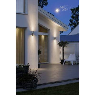 A modern house with an illuminated terrace at night. The moon shines in the sky. Potted plants and a single chair are visible.