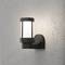 A contemporary external wall light made of black metal with white glass, mounted on a grey wall, emits soft light.