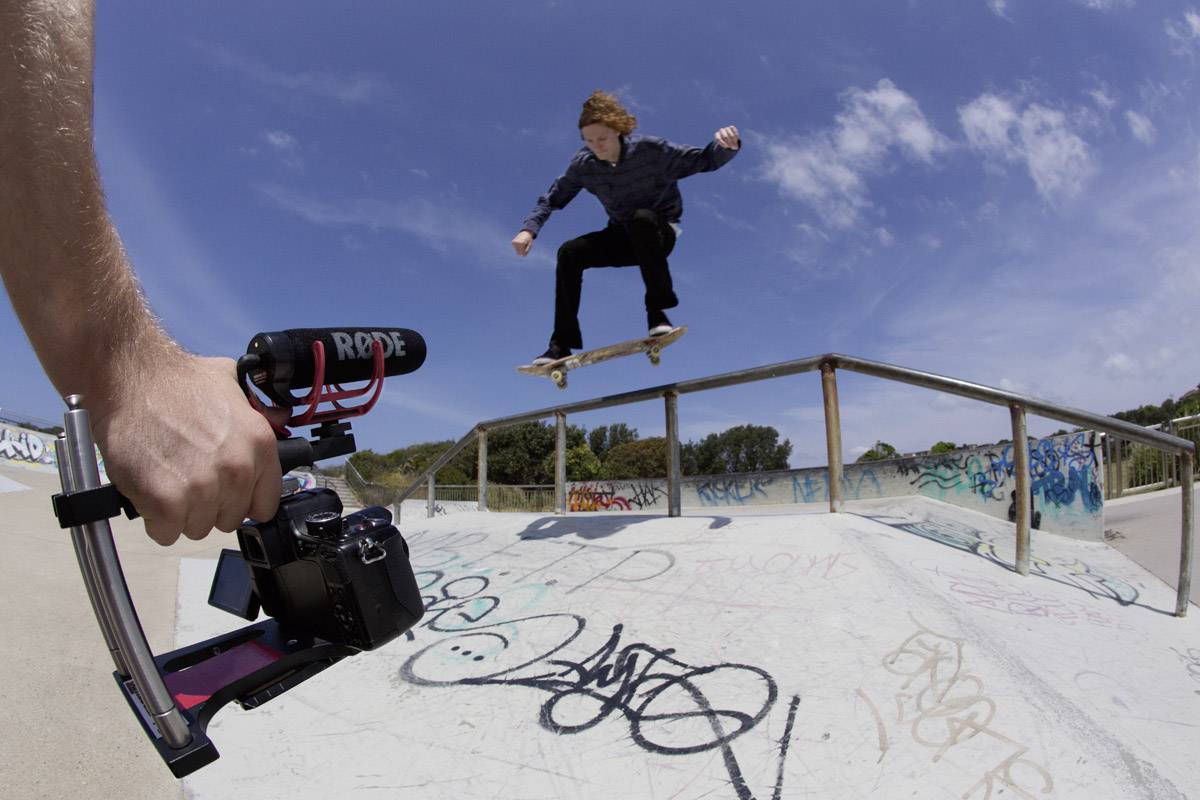 A person is riding a skateboard along a railing in a skate park, while a cameraman films the scene.