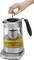 Electric kettle with an integrated teapot, one hand pressing the plunger downwards. Contains a tea strainer with yellow tea.