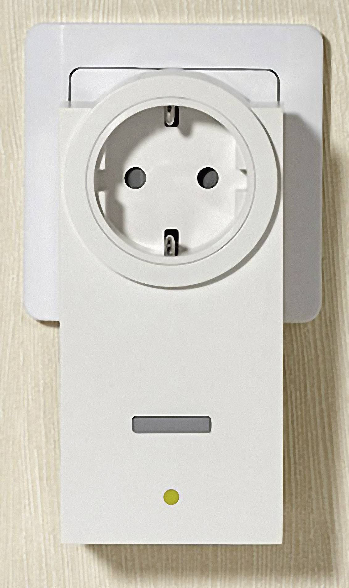 Electrical socket equipped with a smart plug, showing an LED indicator below. Background of light-coloured wood.