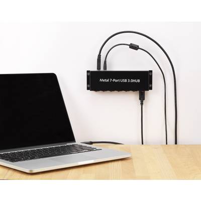 Laptop on a wooden table connected to a black metal seven-port USB hub. Two USB cables are plugged in.