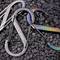 Two S-Carabiners by Nite Ize, one metallic grey, the other iridescent and colourful, lie on a black background.