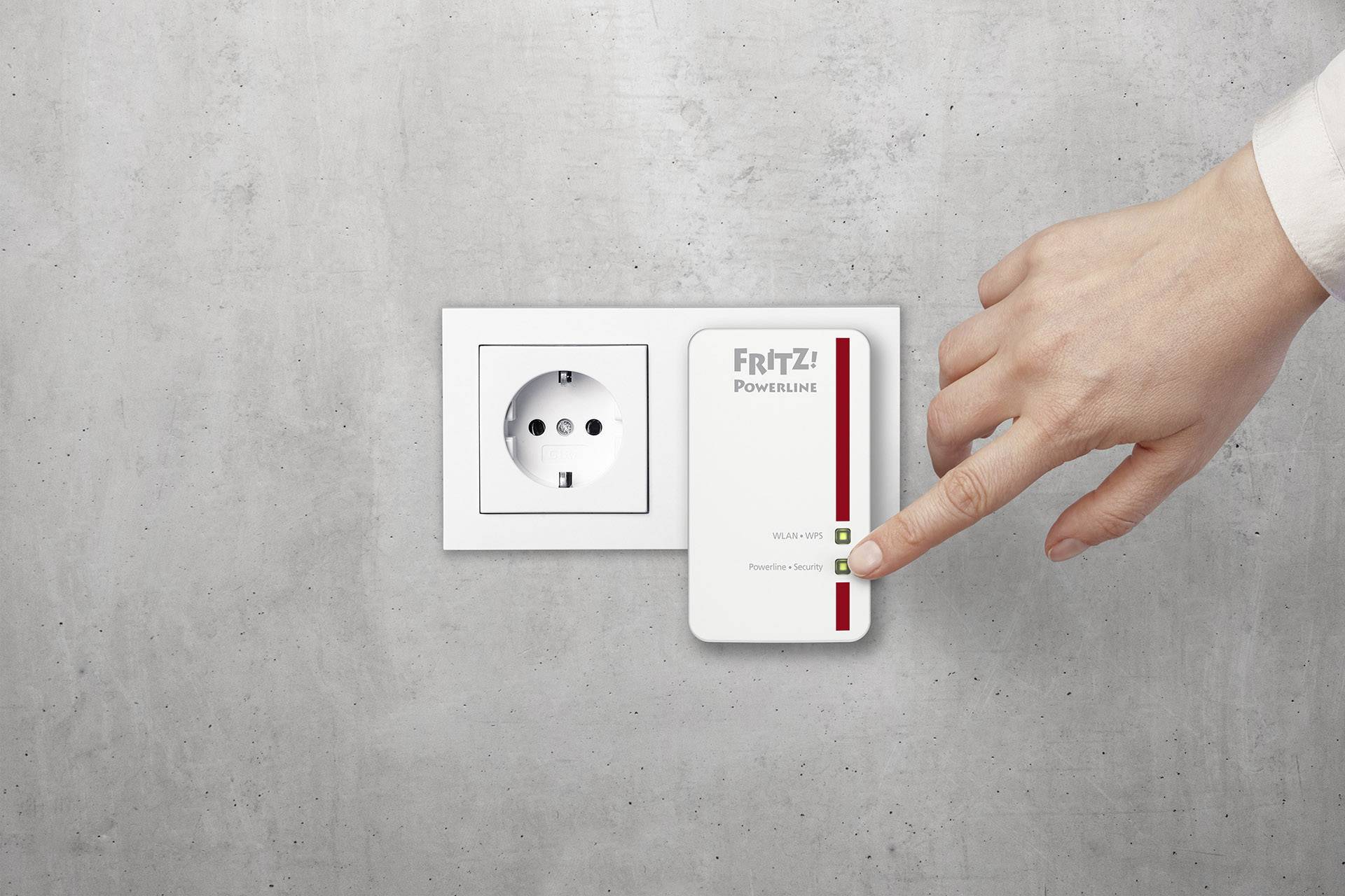 A hand touches a white FRITZ! Powerline adapter plugged into a wall socket.