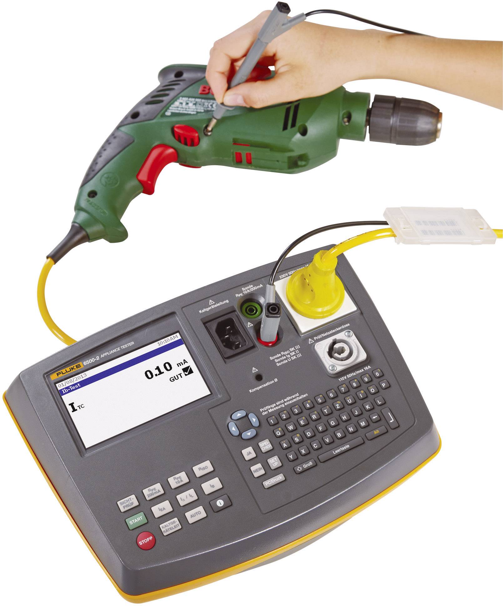 A hand is testing a green drill with a portable electrical testing device. The display shows a measured value and offers button inputs.