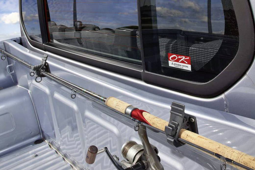 Fishing rod mounted in a holder on the loading bay of a silver pick-up truck.