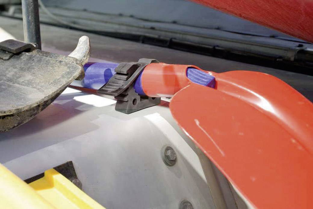 Red and blue shovels, clamped to a vehicle roof rack. Close-up of the mounting. Surroundings suggest outdoor activities.
