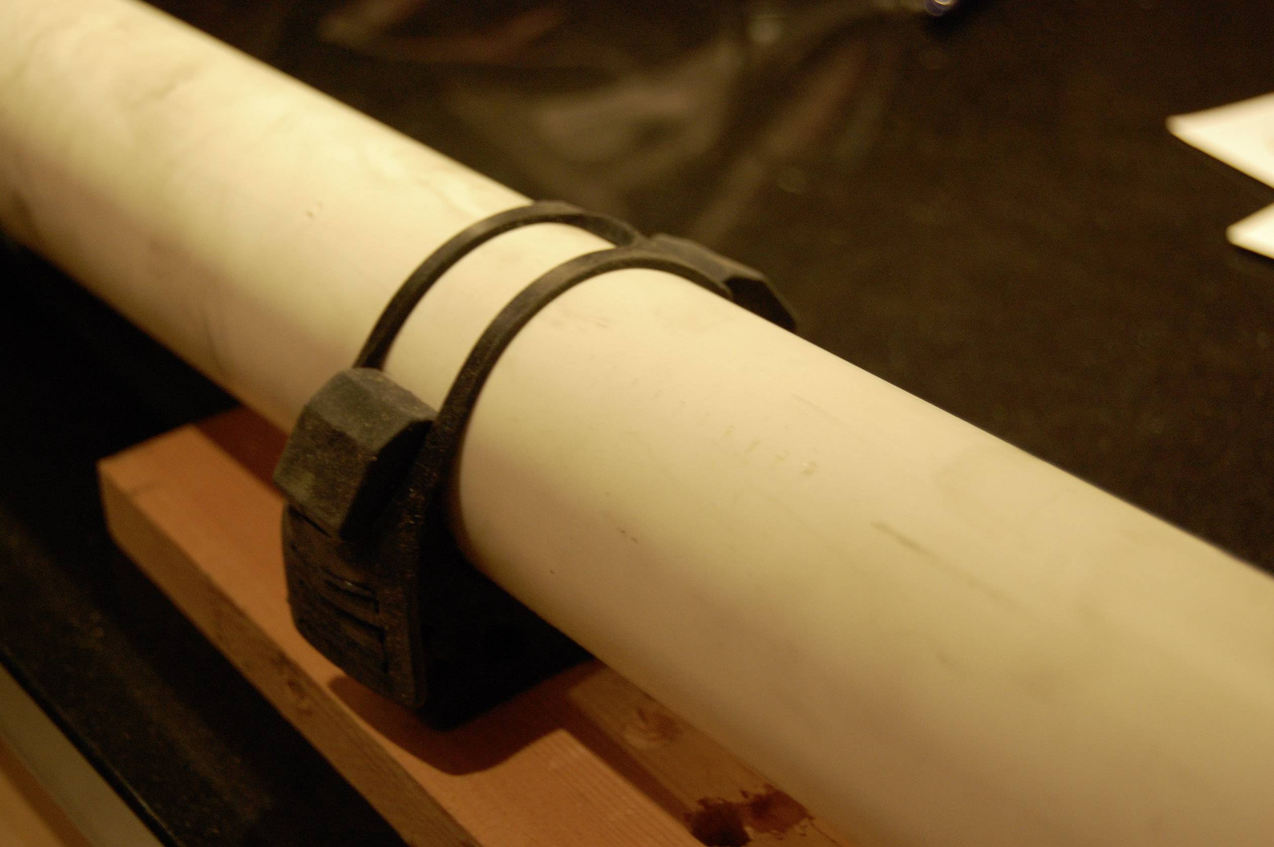 A white pipe, secured with a black plastic clip, is resting on a wooden beam.
