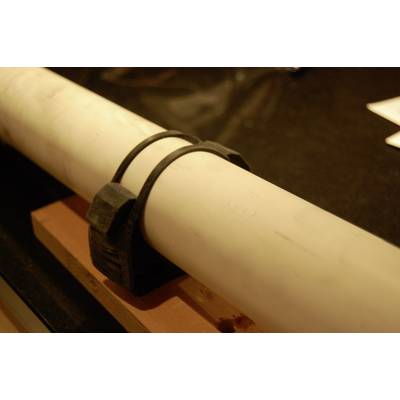 A white pipe, secured with a black plastic clip, is resting on a wooden beam.