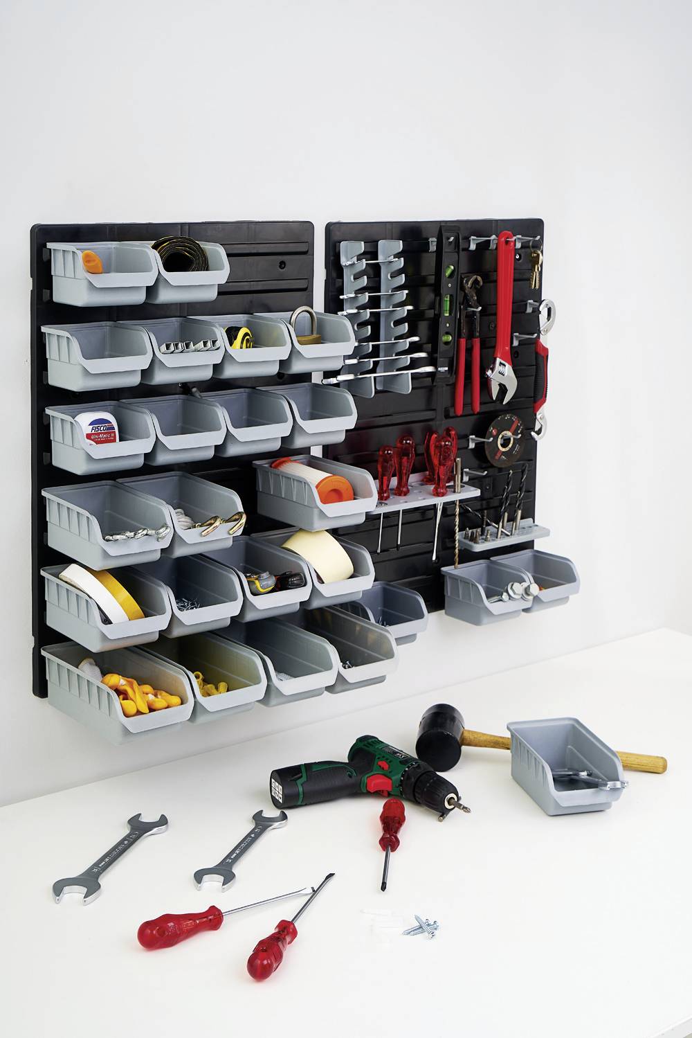 Tool wall with black panels, featuring various grey containers and hooks with tools such as screwdrivers and hammers. Additional tools are lying on the table.