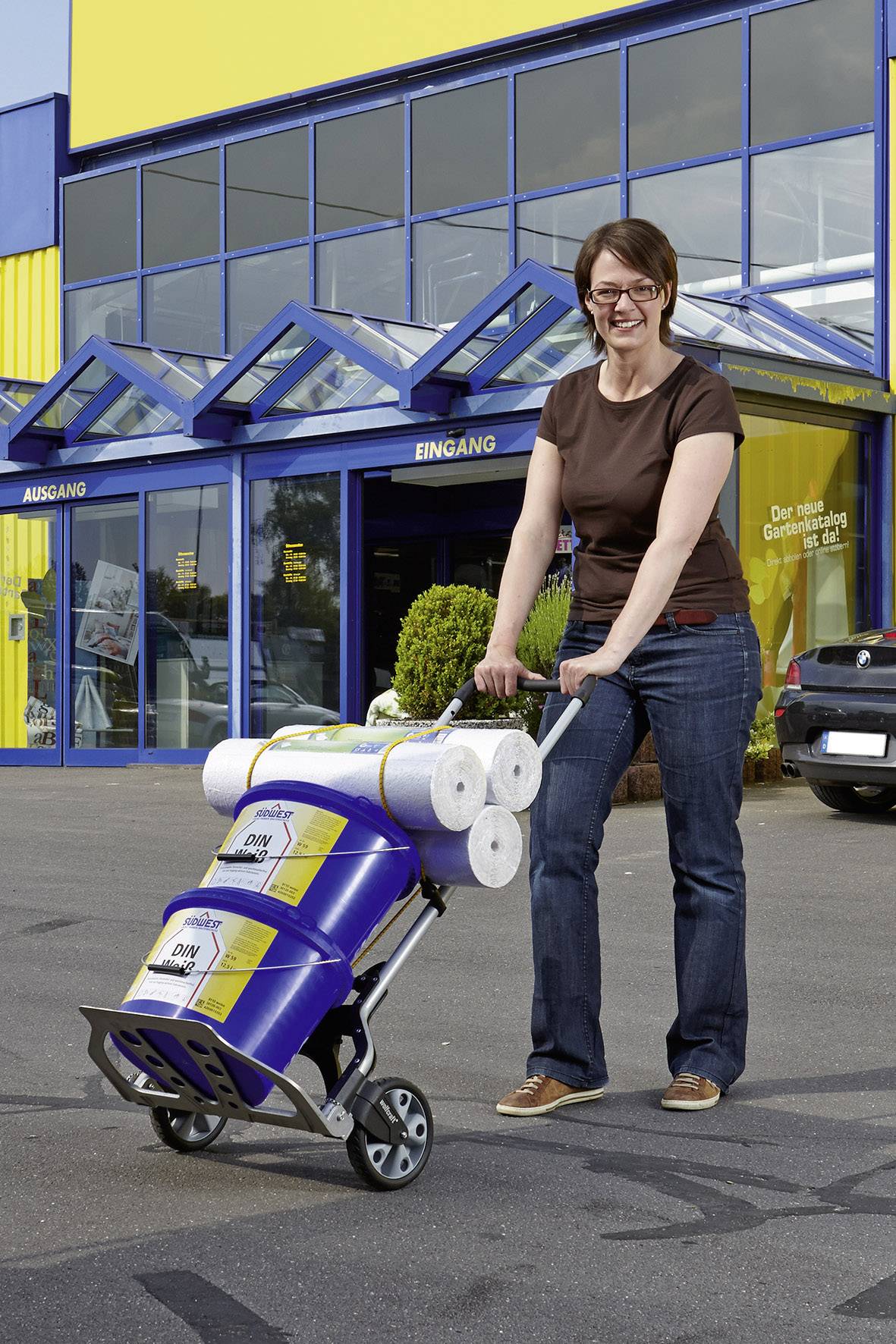 A woman is pushing a loaded shopping trolley in front of a large DIY store with a blue and yellow facade.