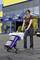 A woman is pushing a loaded shopping trolley in front of a large DIY store with a blue and yellow facade.