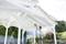 A person is painting the white wooden framework of a carport outdoors using a spray device. A ladder stands nearby.