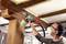 A man is wearing safety glasses and a mask while using a paint sprayer to coat a wooden ceiling in a room.