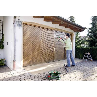 A person is spraying paint onto a garage door using a spray gun. The garage door is masked with protective film. A ladder is standing in the background.