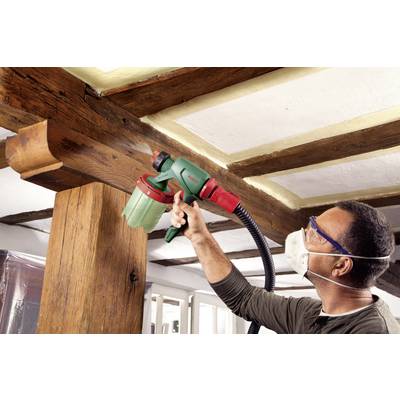 'Man wearing safety glasses and a mask spray-paints a wooden beam using a paint spraying system indoors.'