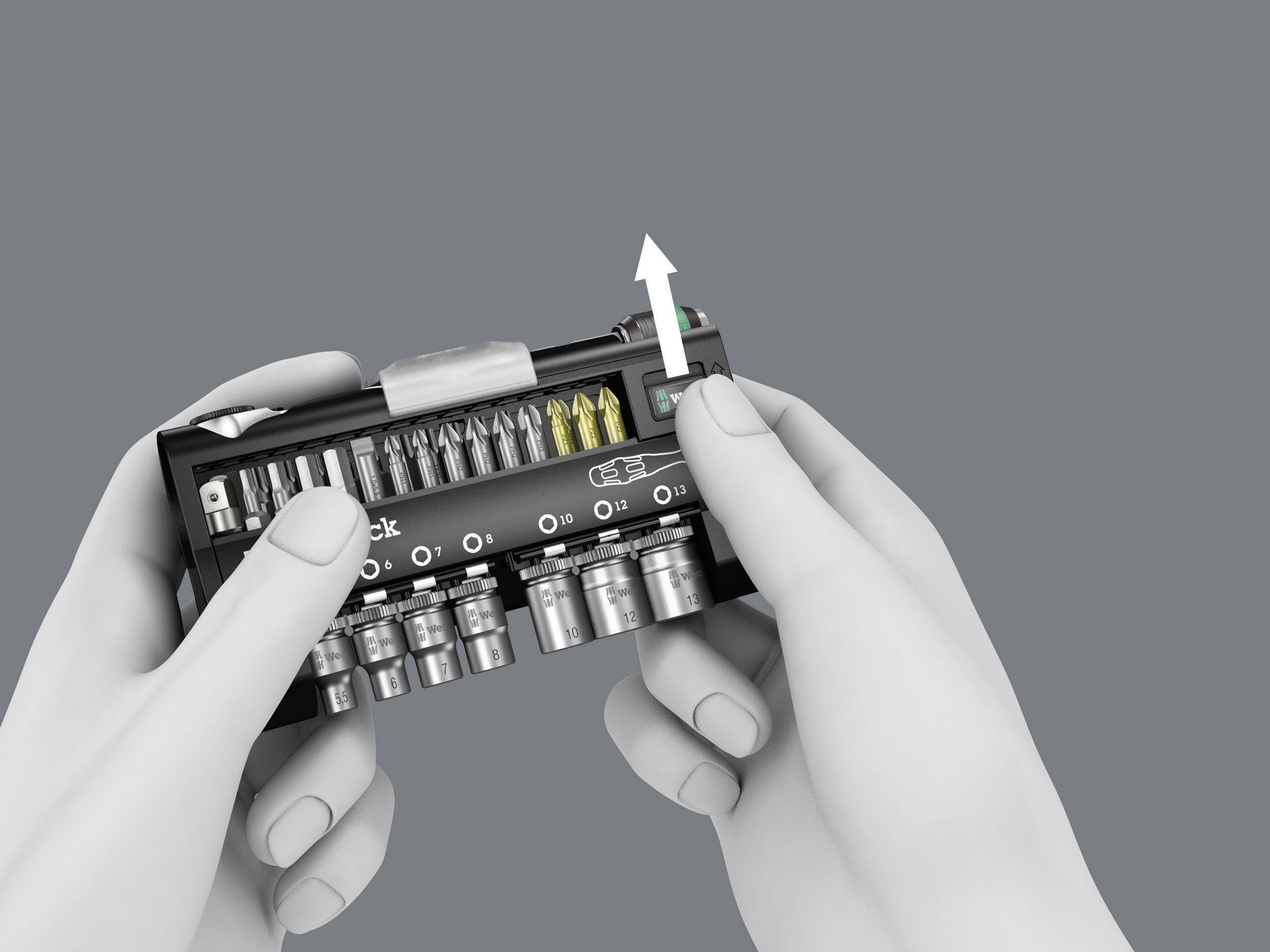 Two hands are holding a black tool set with various attachments, a white arrow pointing to a button in the top right of the set.