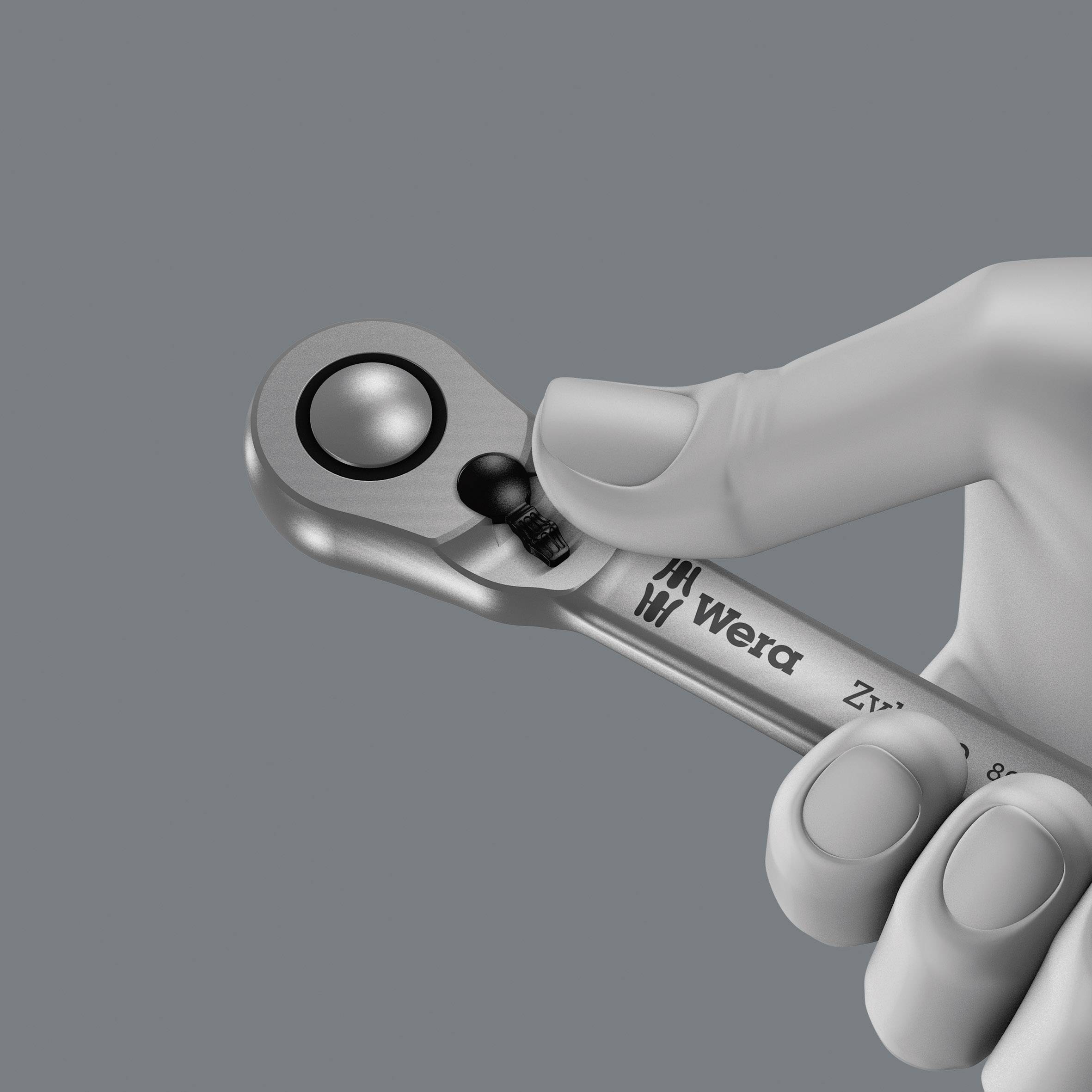 A silver metal ratchet ring with a black button, held by a hand. Inscription 'Wera'.