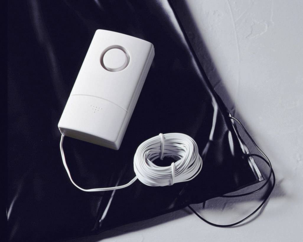 A white electric doorbell with an attached cable lies on a black surface.