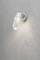 Metal exterior lamp with glass cover mounted on a grey concrete wall. It is switched on and casting a soft light.