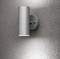 Wall light in a modern design, cylindrical, made of metal, mounted on a textured wall. Light radiates upwards and downwards.