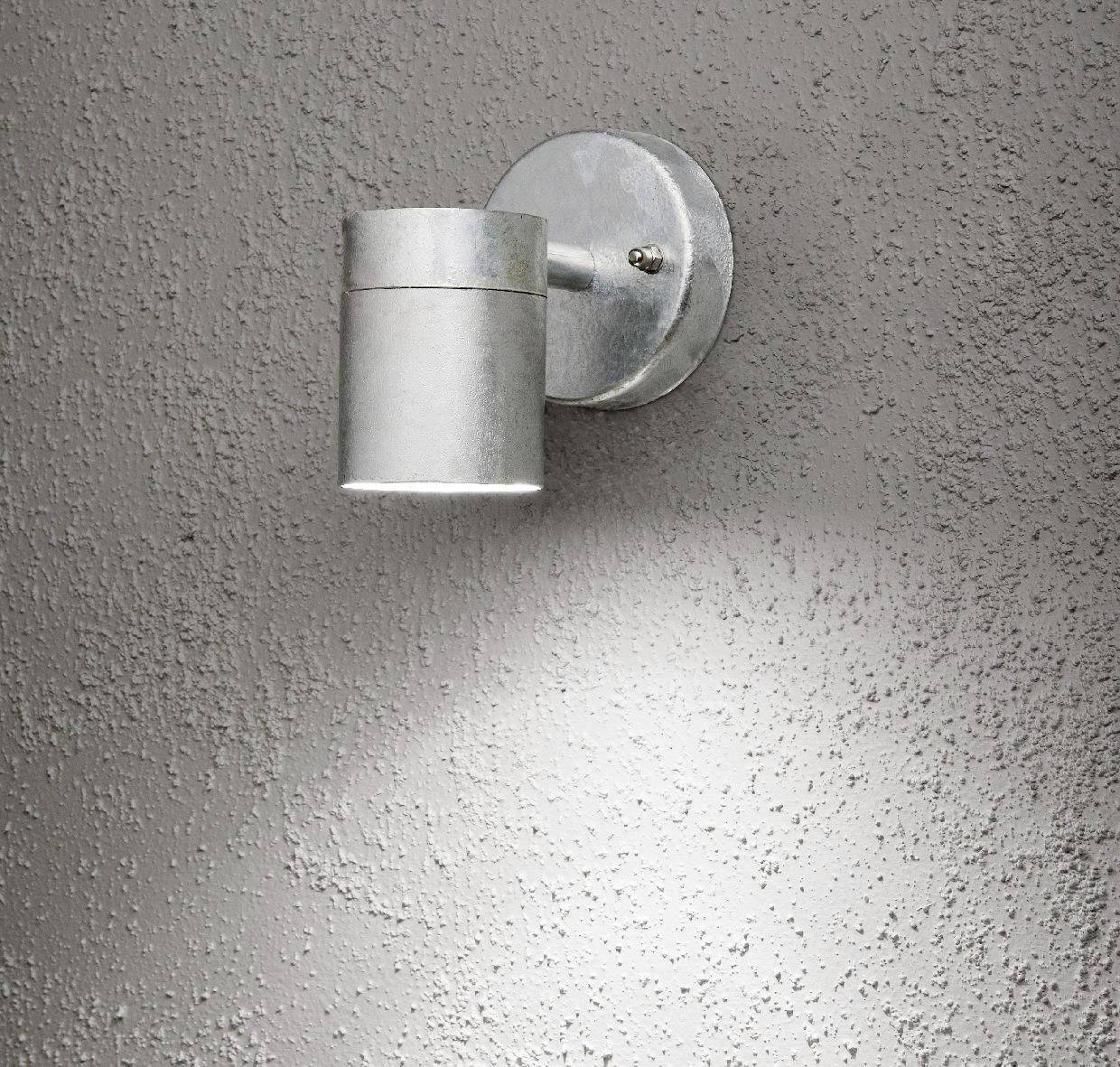 A silver exterior light on a grey wall, casting light downwards.