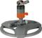 A grey, round lawn sprinkler with orange accents. It has an adjustable head for water distribution in the garden.