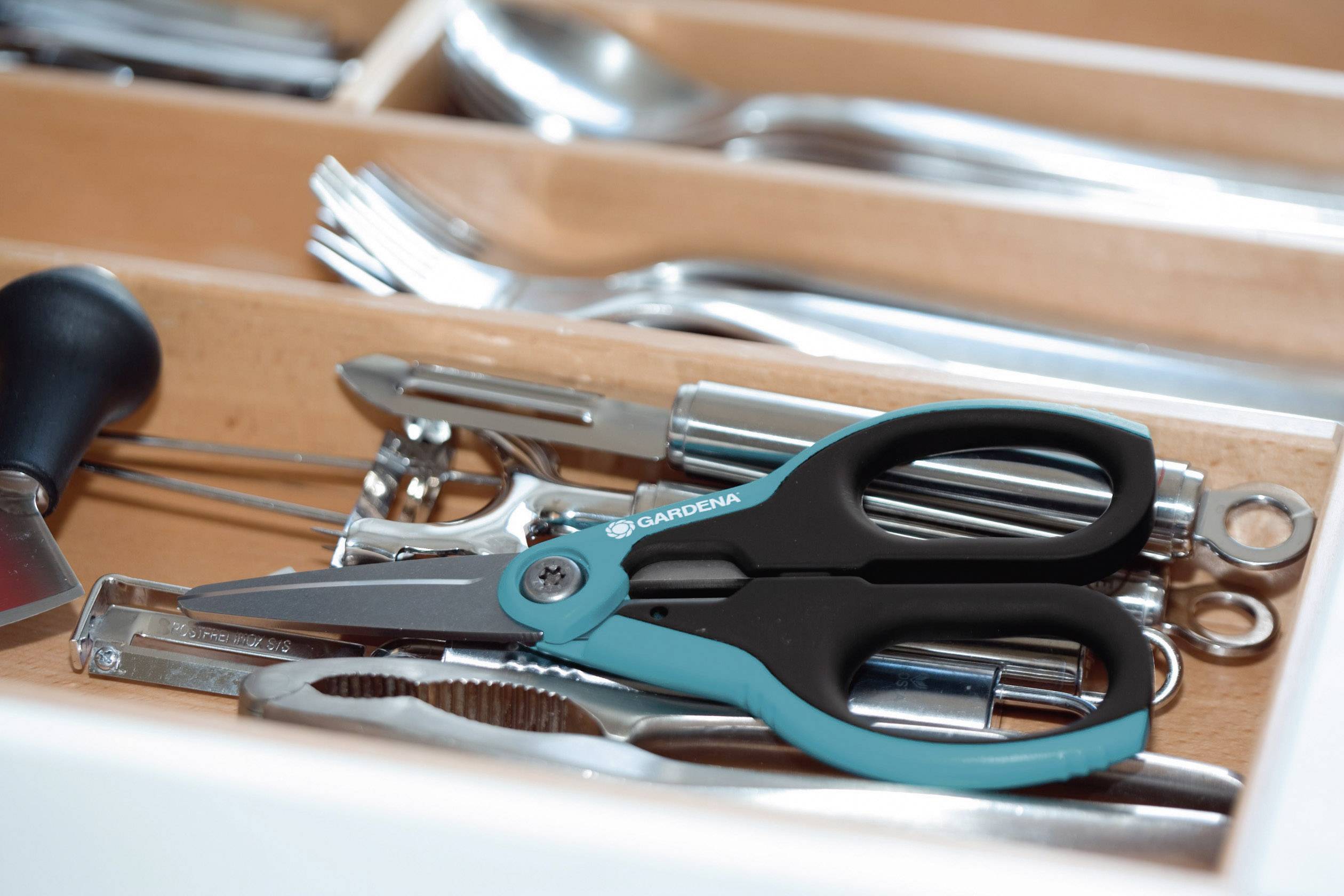 A drawer with various kitchen utensils such as scissors, corkscrew and spoon, neatly arranged in compartments.