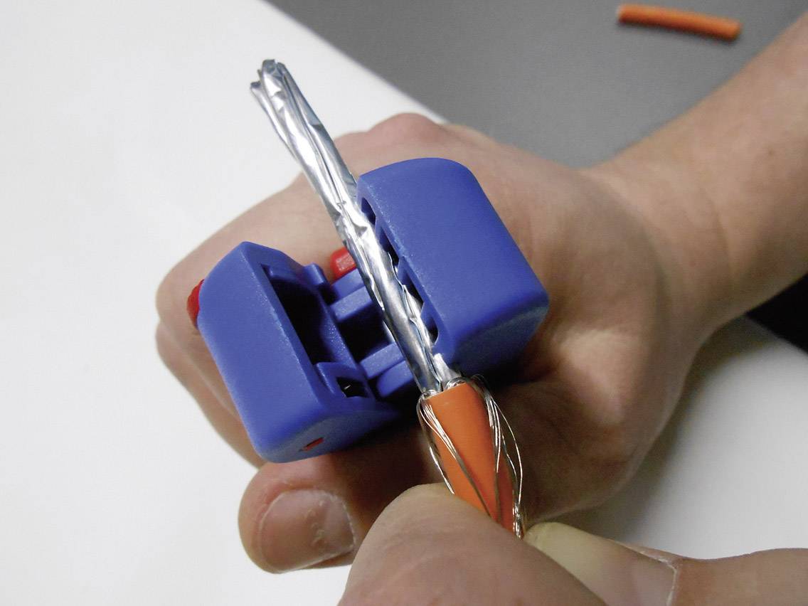 A person is holding a blue tool that is removing wire insulation from an orange cable.