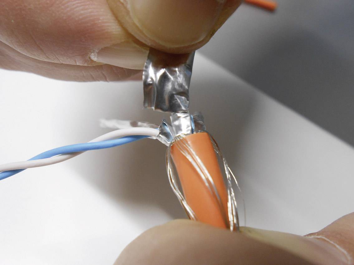 A person is demonstrating the stripping of an orange cable, revealing the silver protective foil underneath.