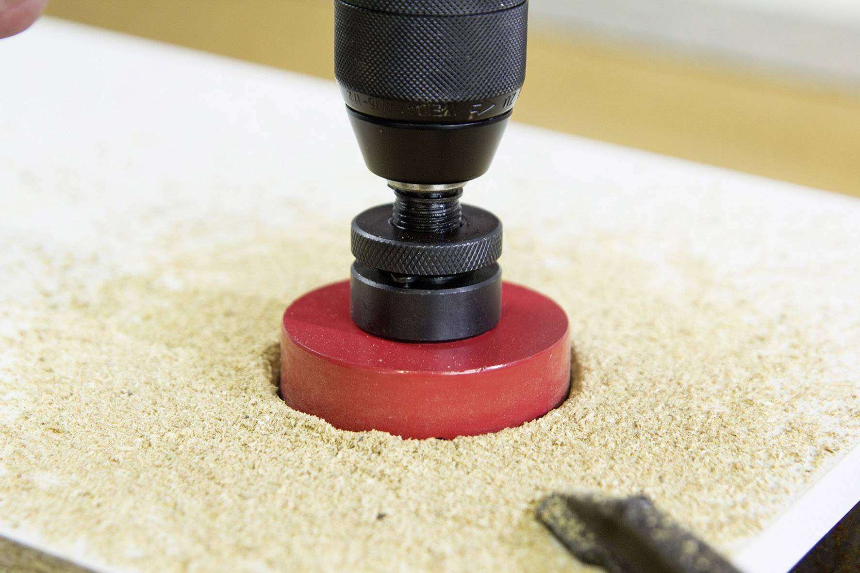 'Drill with hole saw attachment cutting a round hole in wooden board, surrounded by sawdust.'