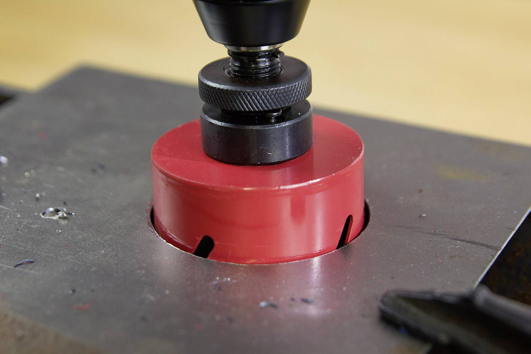 Drill with a red hole saw precisely cutting a circular hole in a metal plate. Close-up shows the work process.