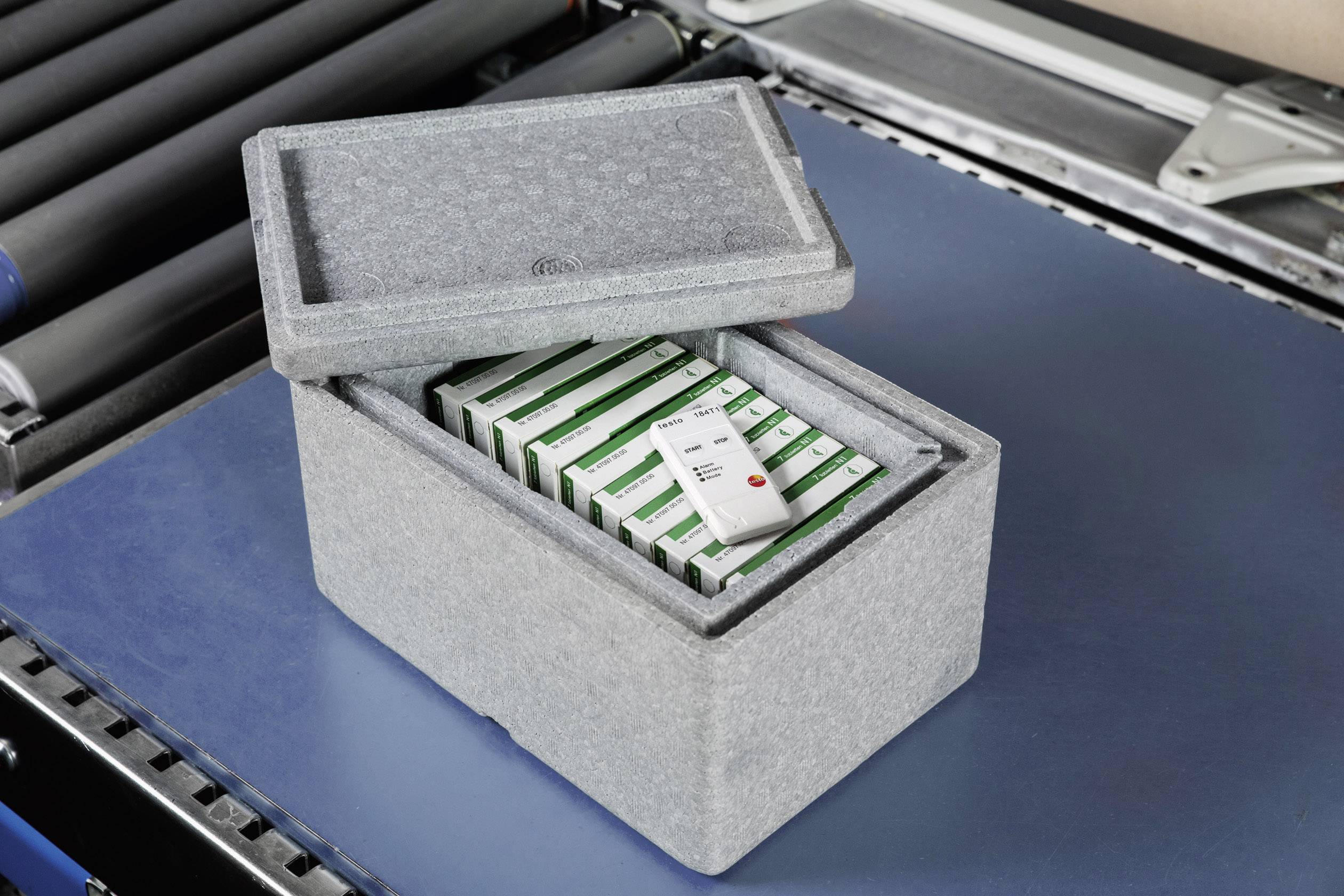 A grey insulated box with an open lid contains stacked medication boxes. One pack is lying on top.