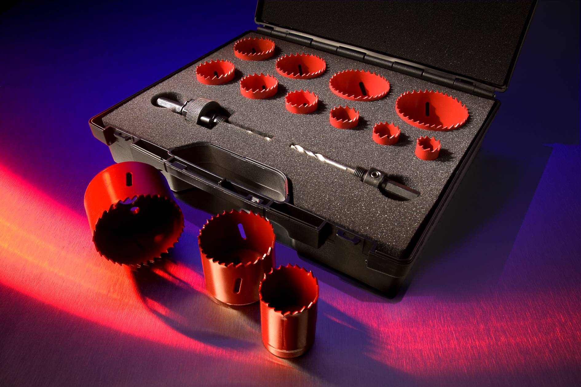 A tool set with several red and black hole saws in various sizes lies in an open black case on a table.