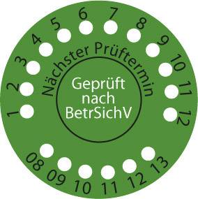 Green verification seal with the inscription 'Tested in accordance with BetrSichV'. Numbers 1 to 12 are arranged in a circular formation.