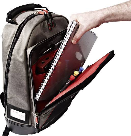 A hand pulls out a notebook from a grey rucksack filled with pens and electronic devices.