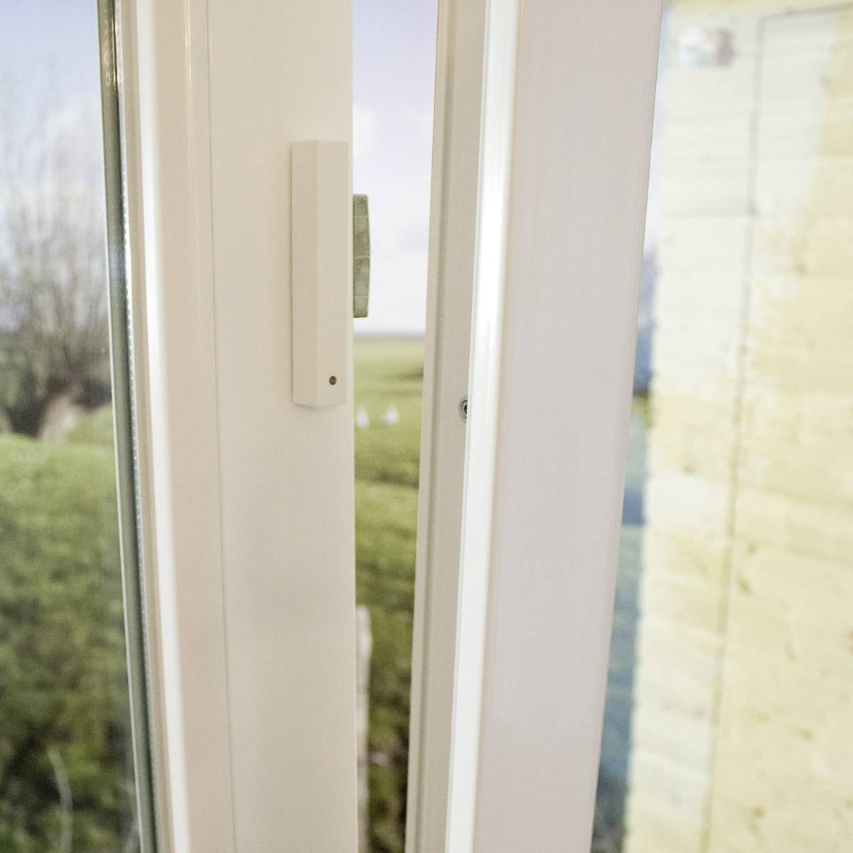 A tilted window with a view of a garden in the background. The window frame is white and the handle is located in the centre.