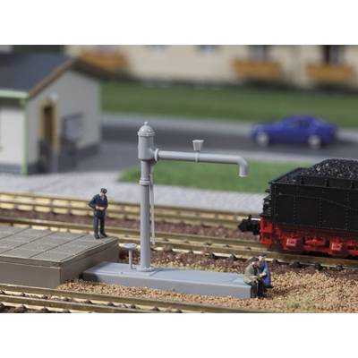 Model railway scene: A steam locomotive is being observed on a track by three figures. A water pump stands at the trackside.